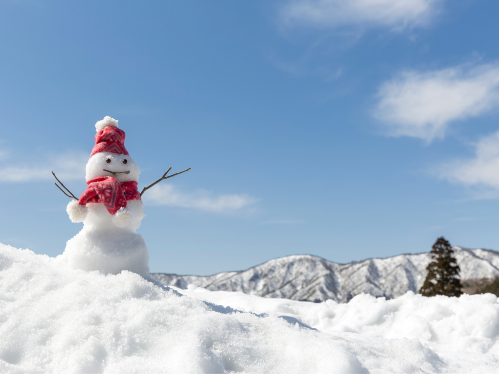 Ways to spend time outdoors: build a snowman. A small snowman with a red hat and scarf sits in front of mountains. 