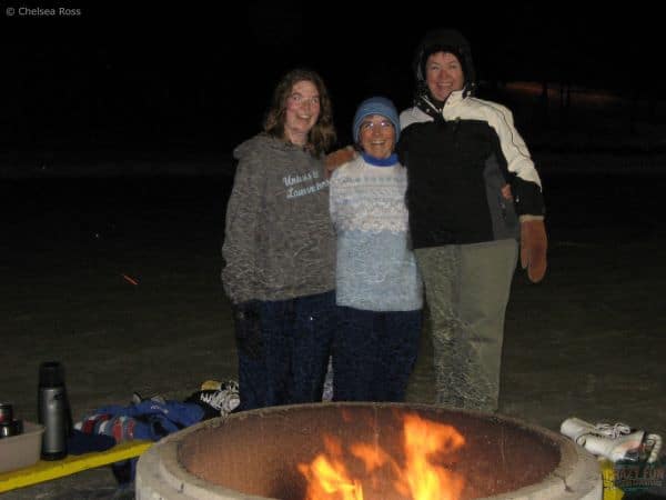 Ways to spend time outdoors: enjoying a fire outside. Ladies standing on bench behind fire. 