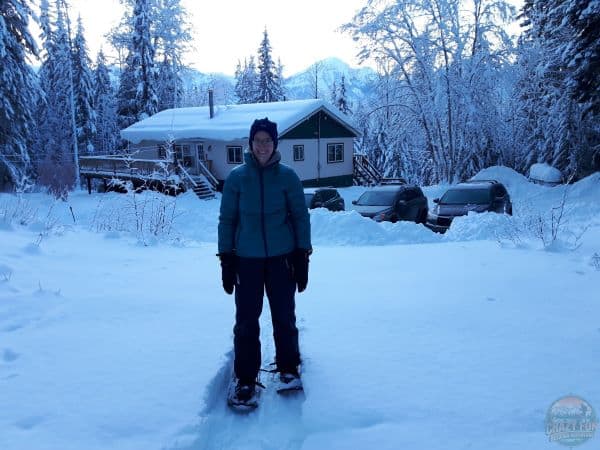 Ways to spend time outdoors: go snowshoeing. Lady snowshoeing in front of a cabin.