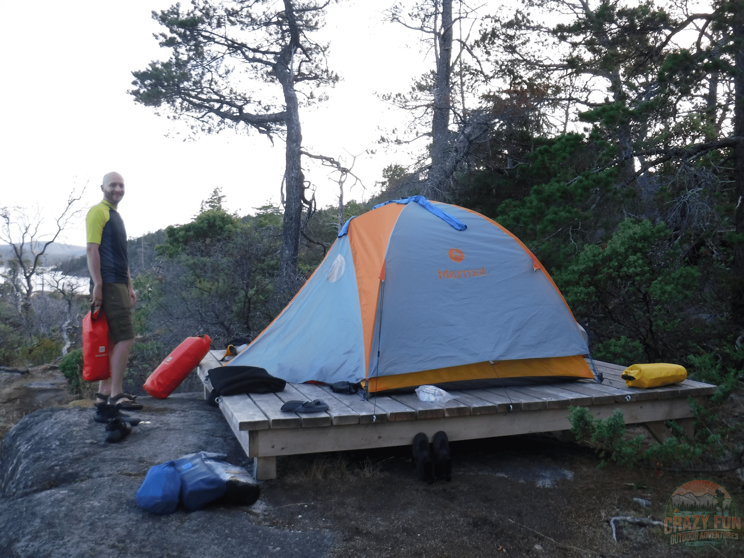Get better at kayaking by doing an overnight trip. Kris is holding a red dry bag in front of our tent.