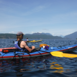 Have an awesome day kayaking with Dad by going on a day trip. Two men are sitting in their kayaks with a beautiful mountain backdrop.