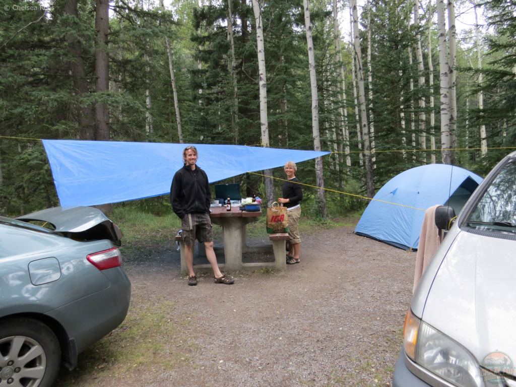 Campsites with showers includes Whistlers campground. A man and women looking this way with a tarp, tent set up. 