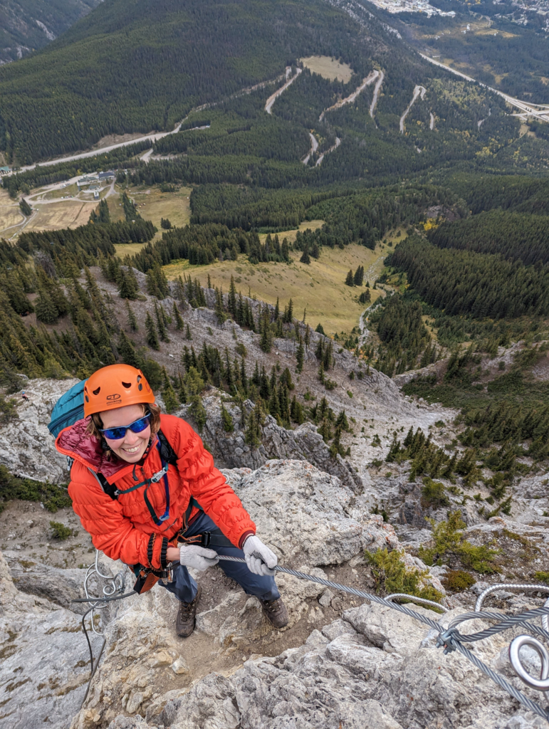 Looking down on a female climbing up the Via Ferrata. Rocks and the valley can be seen down below.