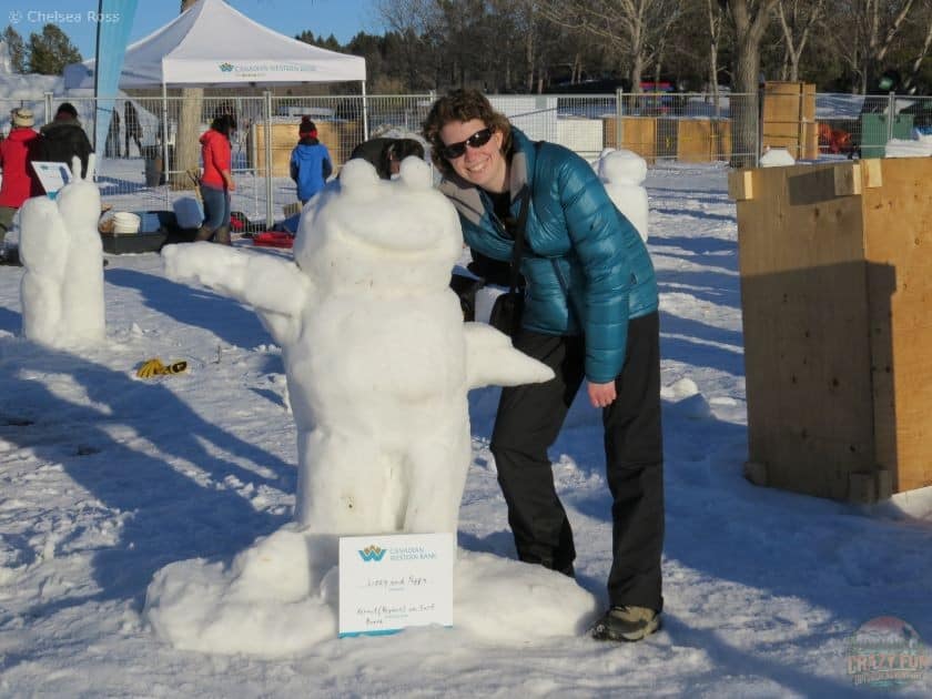 Lady standing near frog snow sculpture. 