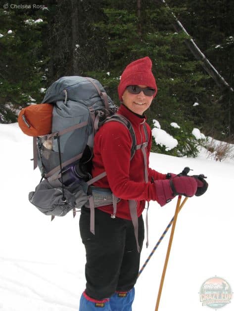 A women wearing her warm red fleece with a pink hat while cross-country skiing with her big backpack to head into our backcountry cabin. 