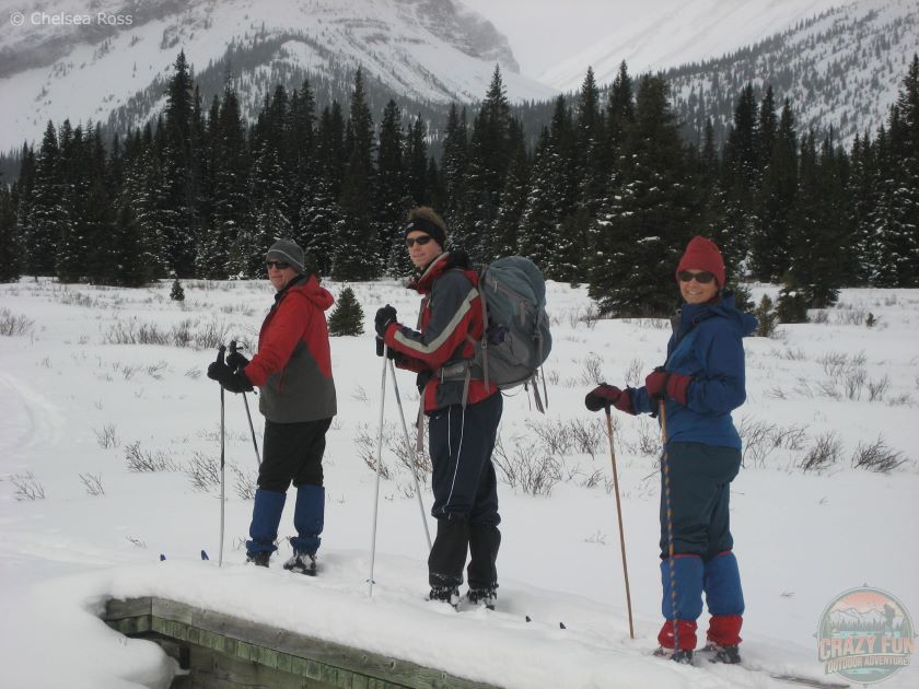 People lined up one behind each other on cross-country skis while wearing gaiters to prevent snow from entering their boots. 