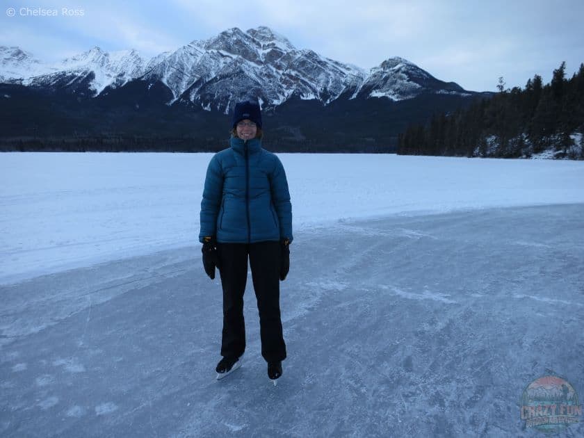 Lady standing on ice with a teal jacket and black pants. Mountains can be seen in the background as well as snow on the ice.