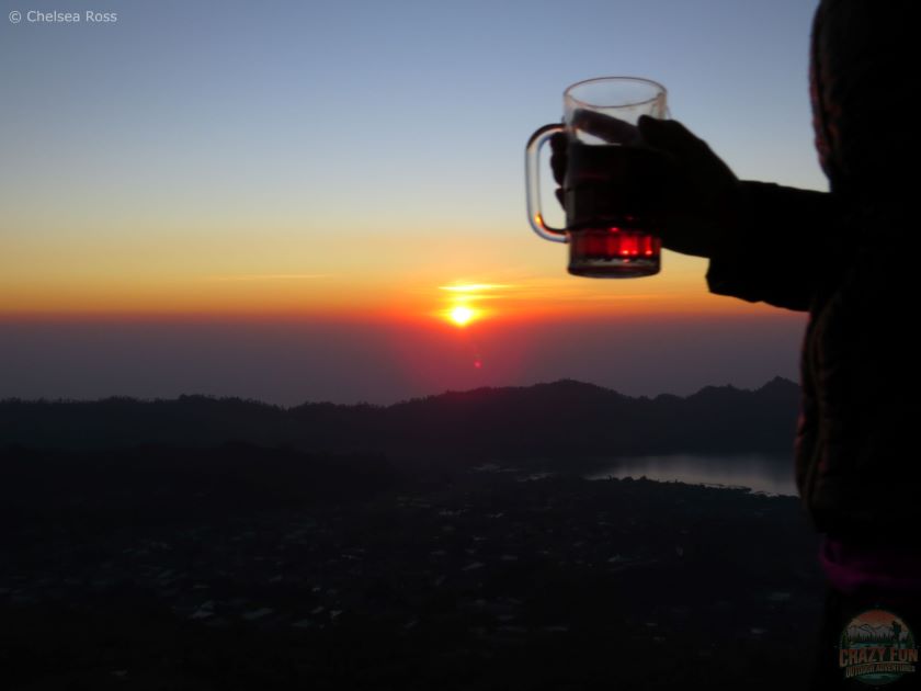 Mount Batur Sunrise Hiking Guide: Breakfast at the Top. The picture shows a person holding tea in a glass that we received for breakfast to warm us up while the sun starts to rise.