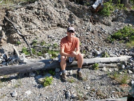 My dad sitting with his salmon merino t-shirt on a log. It's one of the best hiking gifts for Dads.