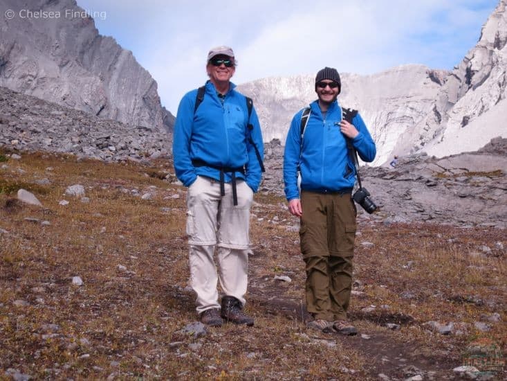 Best Hiking Gifts for Dads: Two men are wearing a blue fleece, standing beside each other with grey mountains in the background. 