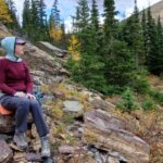 Red and green Minus33 Merino Wool shirts on lady sitting on rock.