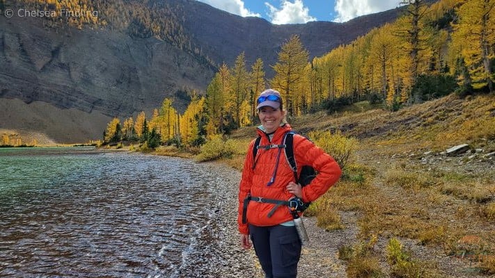 Lady with golden larches behind her at upper Rowe Lake during Waterton fall.