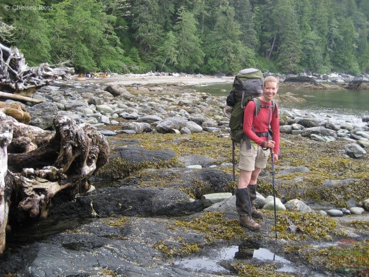 Lady backpacking and standing on rocks and algae with trees and rocks behind her as part of crazy fun outdoor adventures. 