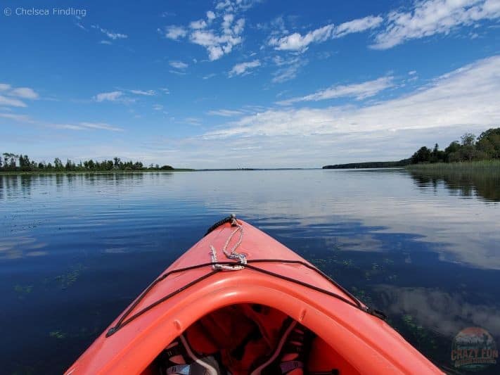 Calm mirrored waters of Lake Isle in Alberta reflecting trees and clouds and the sky.