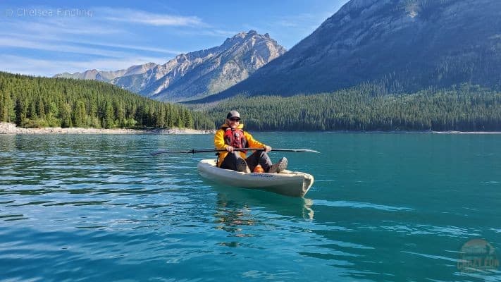 Person sitting on a sit-on-top kayak on turquoise water with a mountain backdrop in Alberta. 