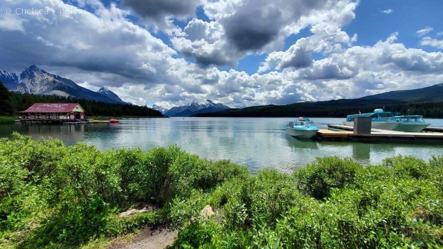 View of the Maligne Lake boathouse and cruise boats under partly cloudy skies in Jasper National Park. 