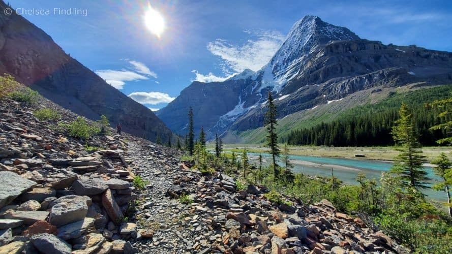 Rocky trail running alongside a turquoise glacial river with Mt. Robson towering in the distance.