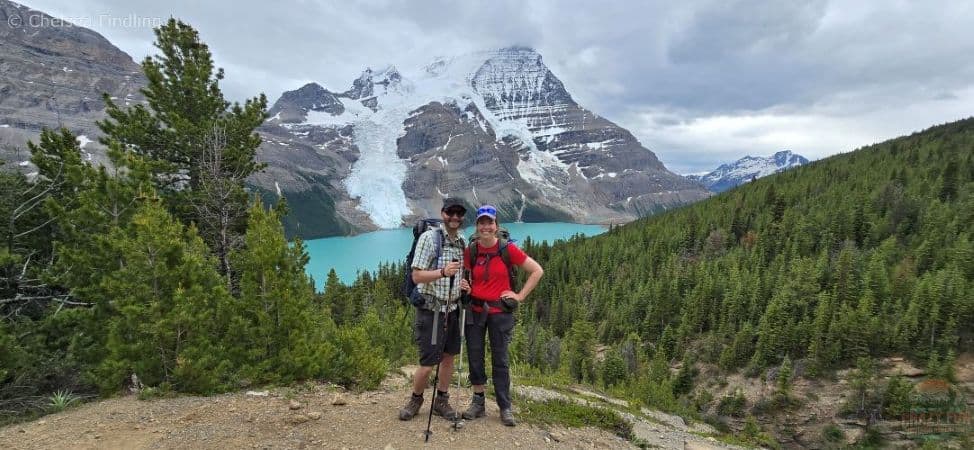 Couple hiking uphill toward Mumm Basin with turquoise Berg Lake visible below.