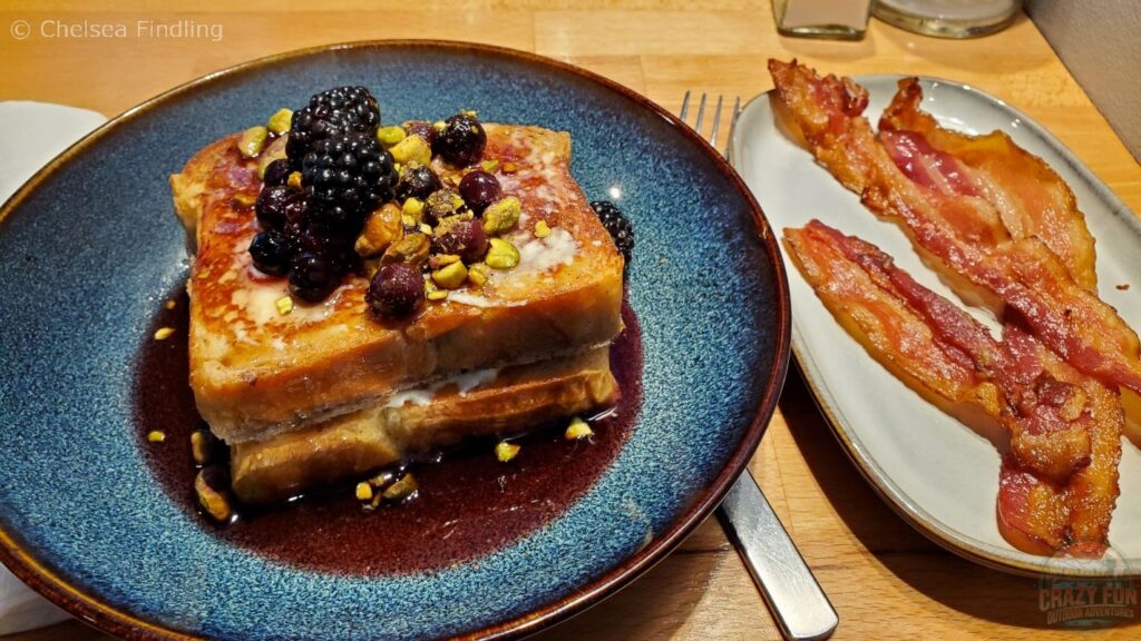 French toast topped with berries and pistachios, served alongside crispy bacon.