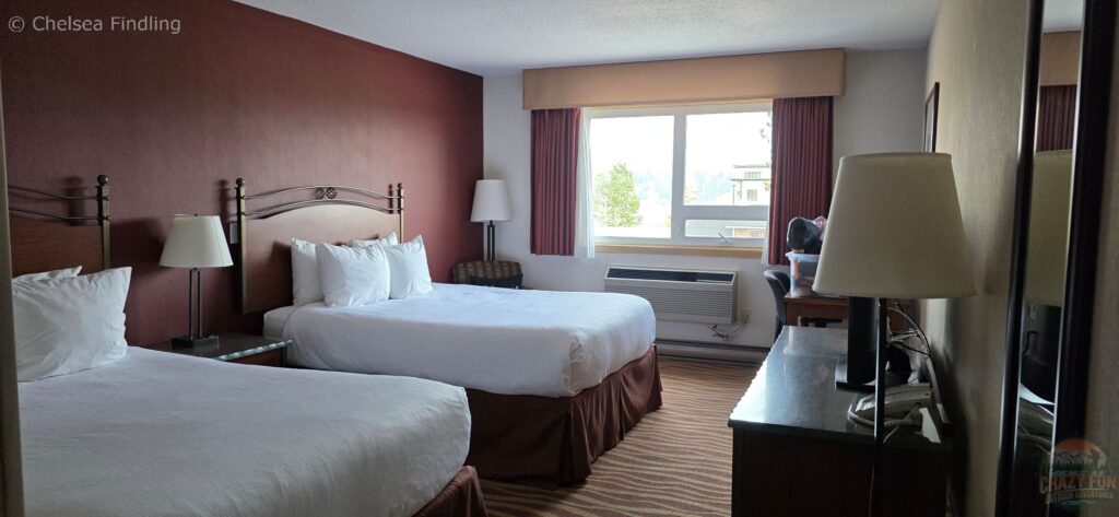 Showing two queen beds inside a guest room at Invermere Inn & Suites, with standard hotel room furnishings and sleeping space.