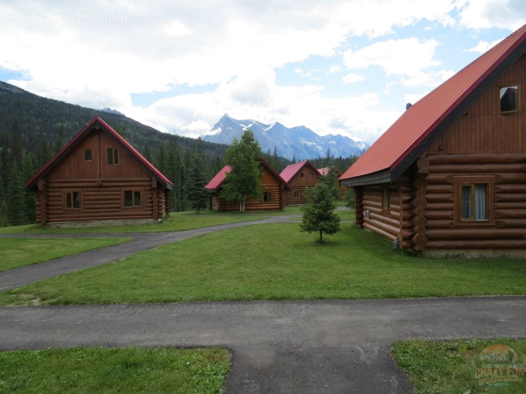 Exterior view of wooden cabin accommodations at Kicking Horse River Chalets surrounded by trees and mountain scenery.