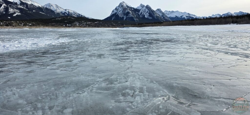 Cloudy, textured ice formations at Preacher's Point with the rugged Rocky Mountains rising behind Abraham Lake.