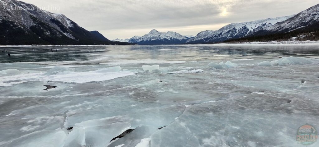 Uneven slabs of ice pushing up against each other along the shoreline of Abraham Lake, forming jagged ridges and textured layers against the rocky banks.