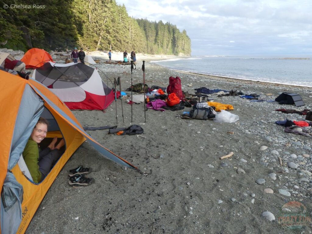 A woman in a Marmot Limelight 3P tent beside an MSR tent on the sand, showcasing essential backpacking gear for a coastal adventure.