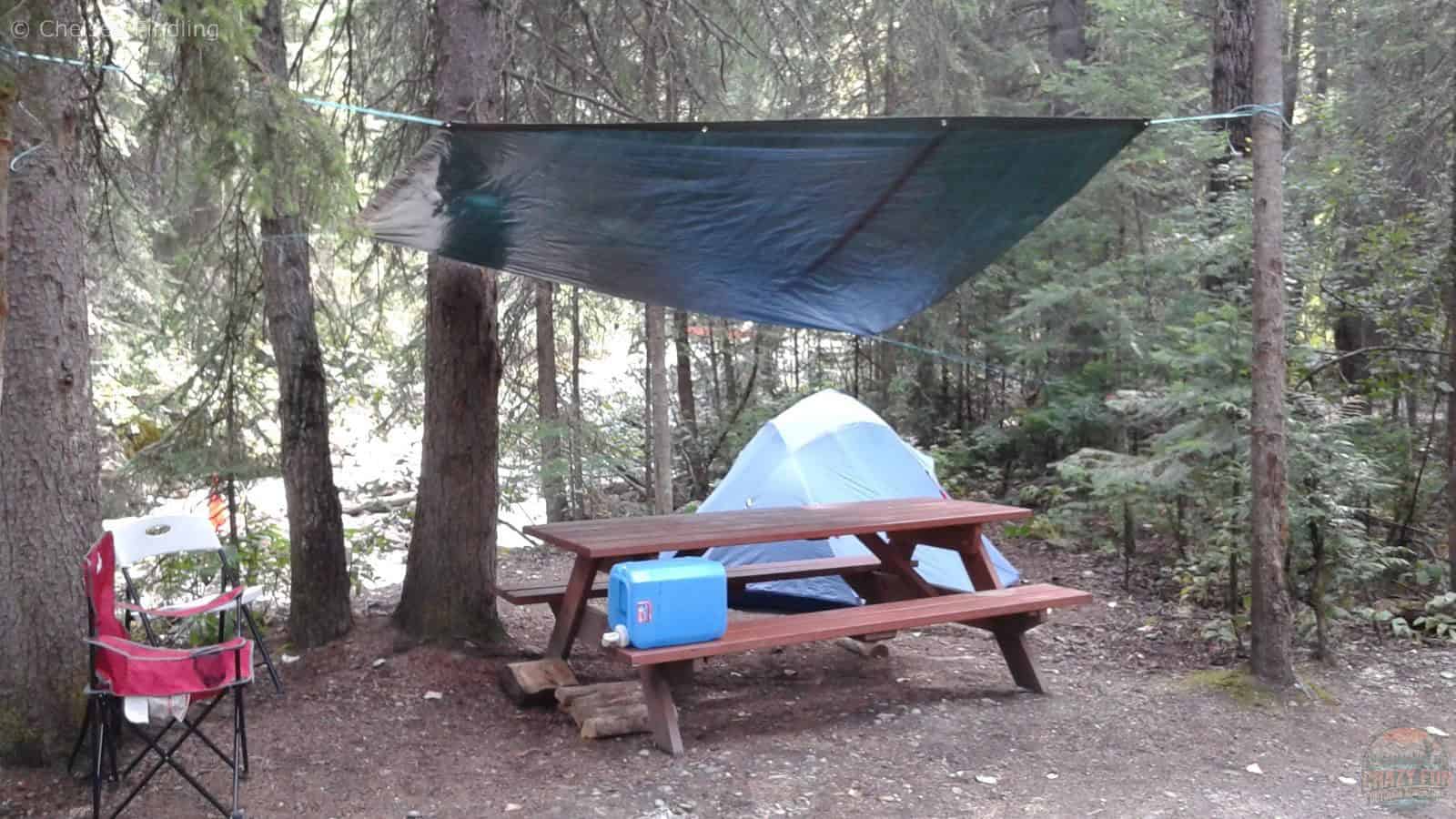 Camping setup with a tarp, tent, camping chair, and outdoor camping gear arranged at a campsite.