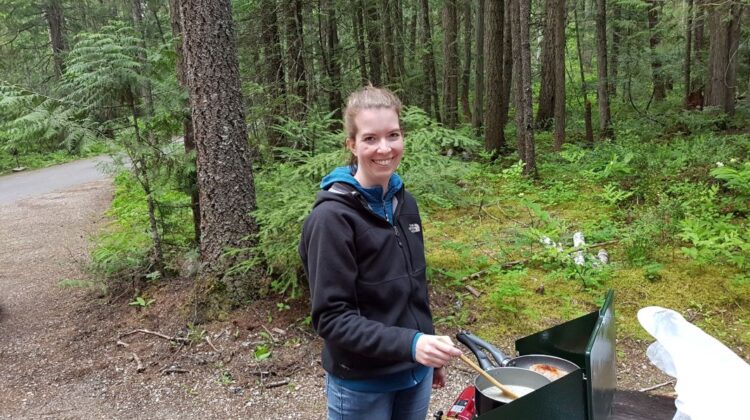 Woman cooking food on a portable camping stove outdoors using her camping gear.