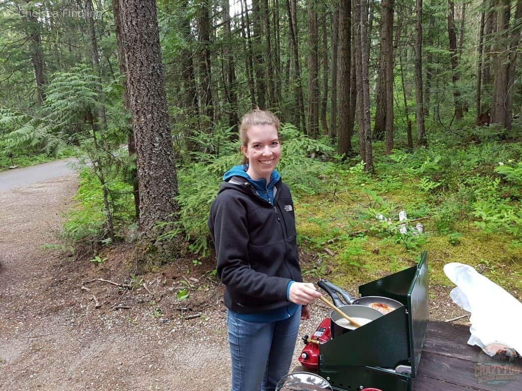 Woman cooking food on a portable camping stove outdoors using her camping gear.