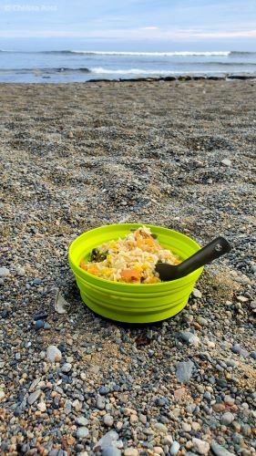 A bowl of polenta cheese stew served for supper on a sandy beach during a backpacking trip.
