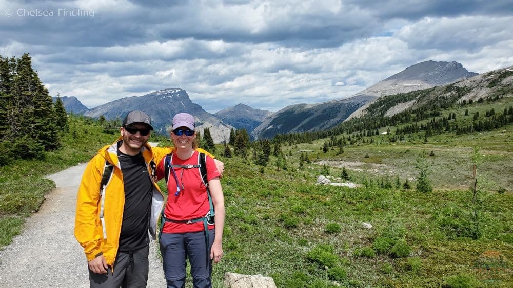 A couple on a hiking trail with mountains in the background.