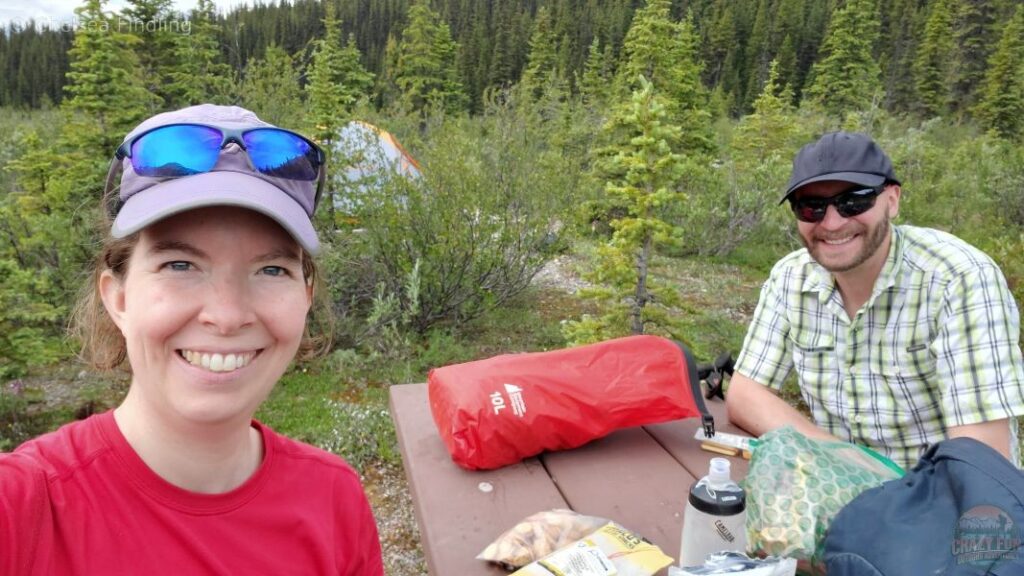 A couple eating lunch at a picnic table at Robson Pass with Mount Robson rising in the background.