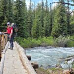 Backpacker crossing a bridge over flowing water near Evelyn Creek campground on the Skyline Trail.