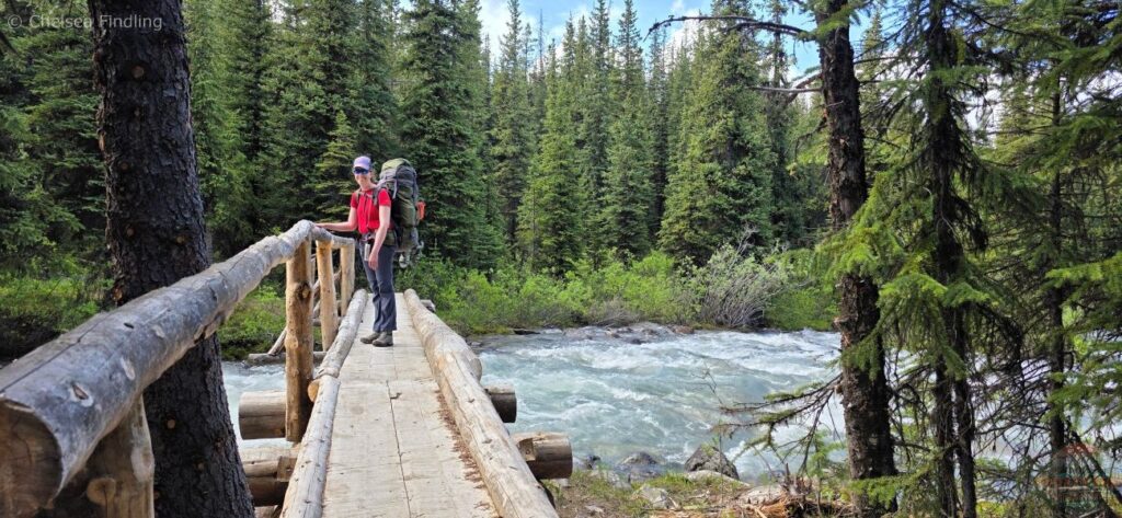 Backpacker crossing a bridge over flowing water near Evelyn Creek campground. 
