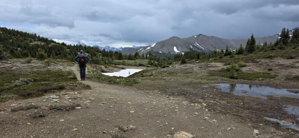 View of a hiker with the trail, mountains and dark clouds in the background. 