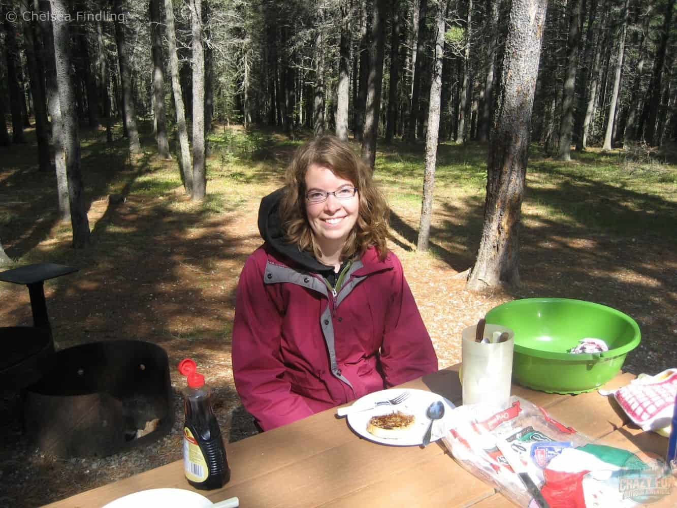 Woman eating a piece of French bread while sitting at a picnic table outdoors.