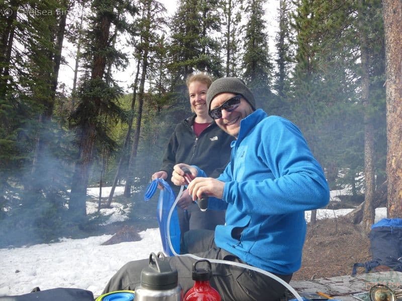 A couple filtering water into a water bladder, showing an essential item from their backpacking gear list for a multi-day hike.