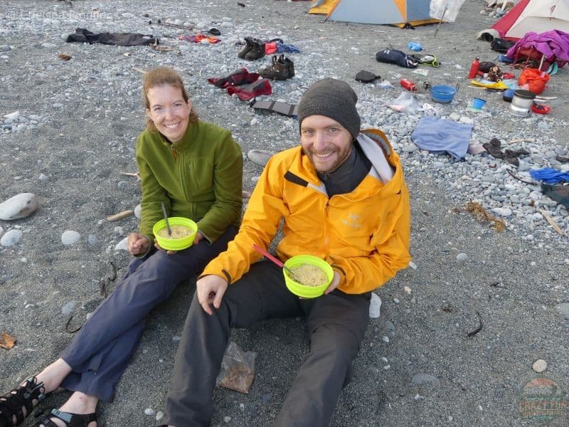 A couple sharing supper on the beach during a cool evening on the West Coast Trail, dressed in layers from a backpacking gear list.
